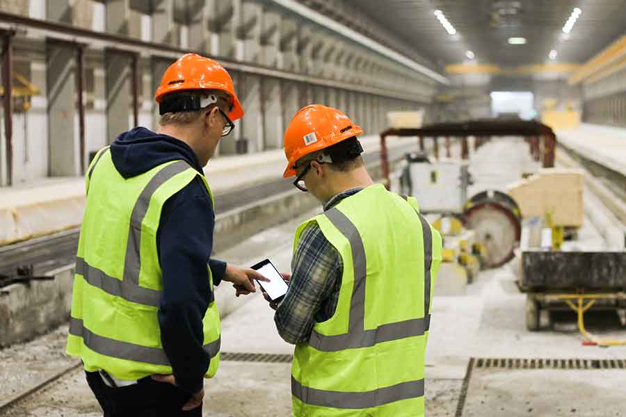 two men in yellow vests and hard hats looking at data on a phone