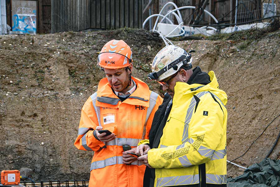 Two men in construction workwear looking at devices